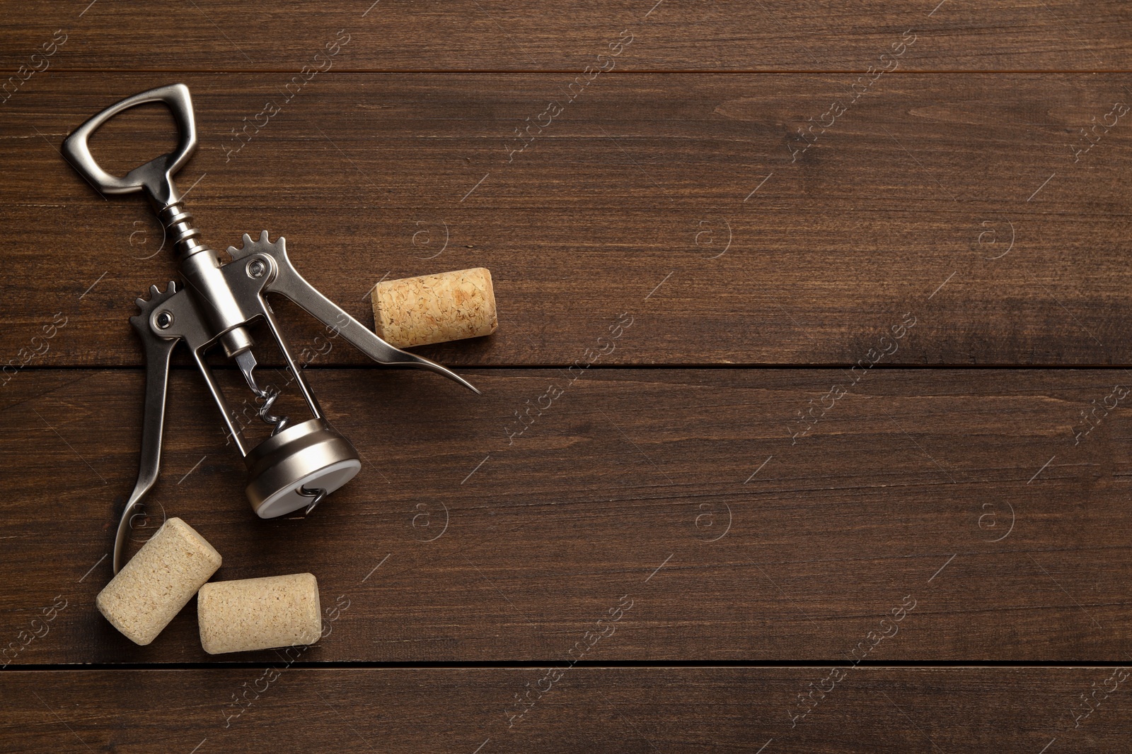 Photo of Wing corkscrew and corks on wooden table, flat lay. Space for text