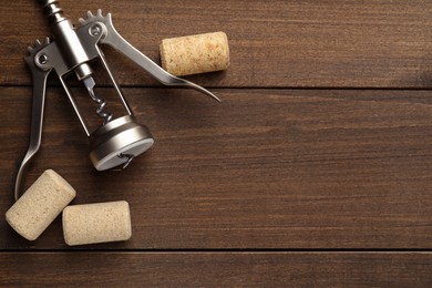 Photo of Wing corkscrew and corks on wooden table, flat lay. Space for text