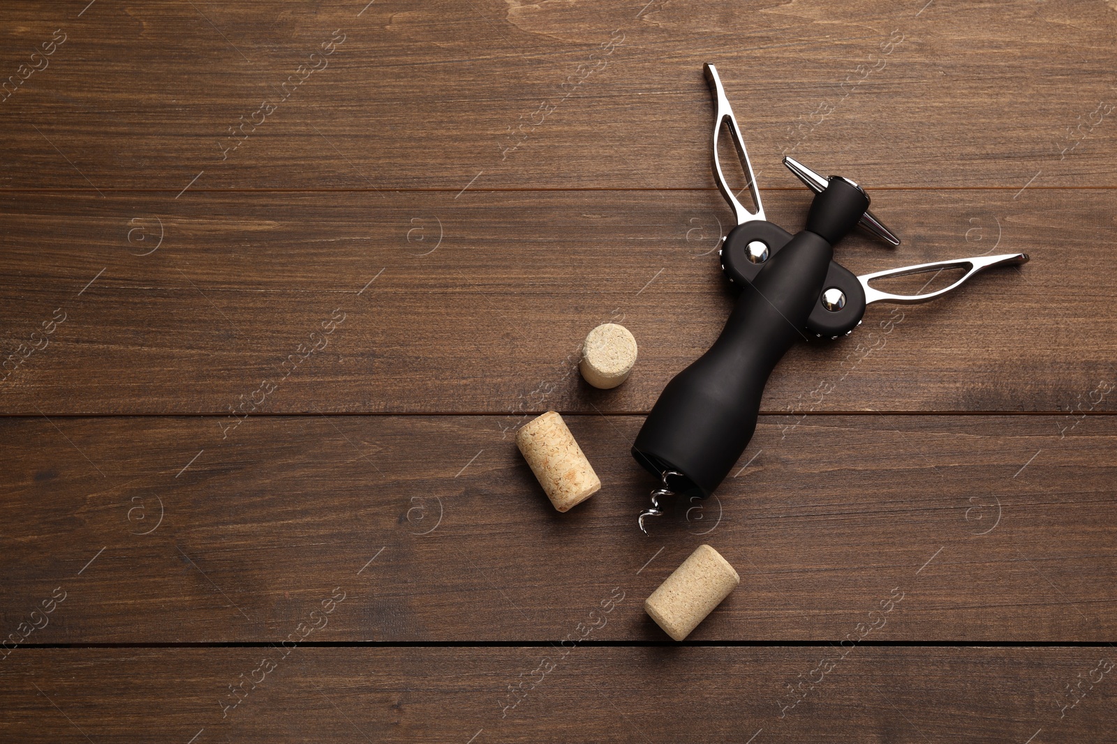 Photo of Wing corkscrew and corks on wooden table, flat lay. Space for text