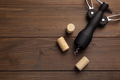 Photo of Wing corkscrew and corks on wooden table, flat lay. Space for text