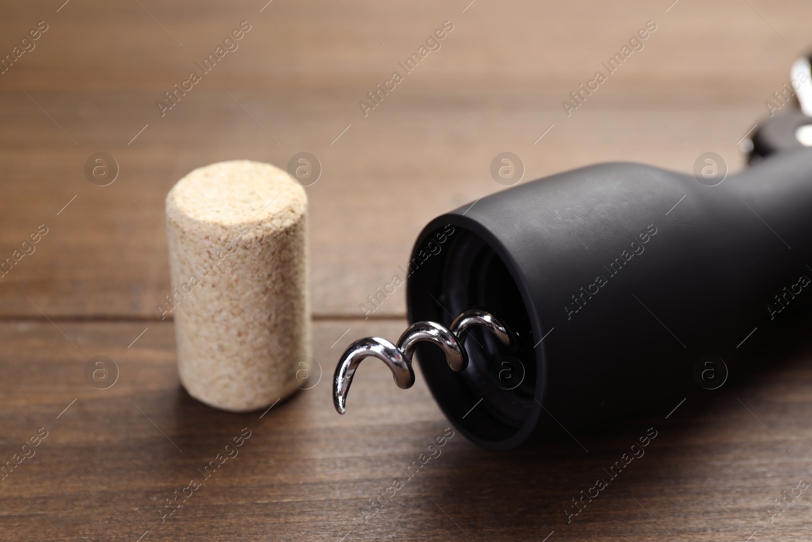 Photo of Corkscrew and cork on wooden table, closeup