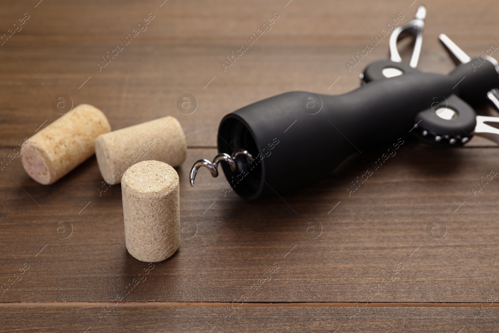 Photo of Wing corkscrew and corks on wooden table, closeup