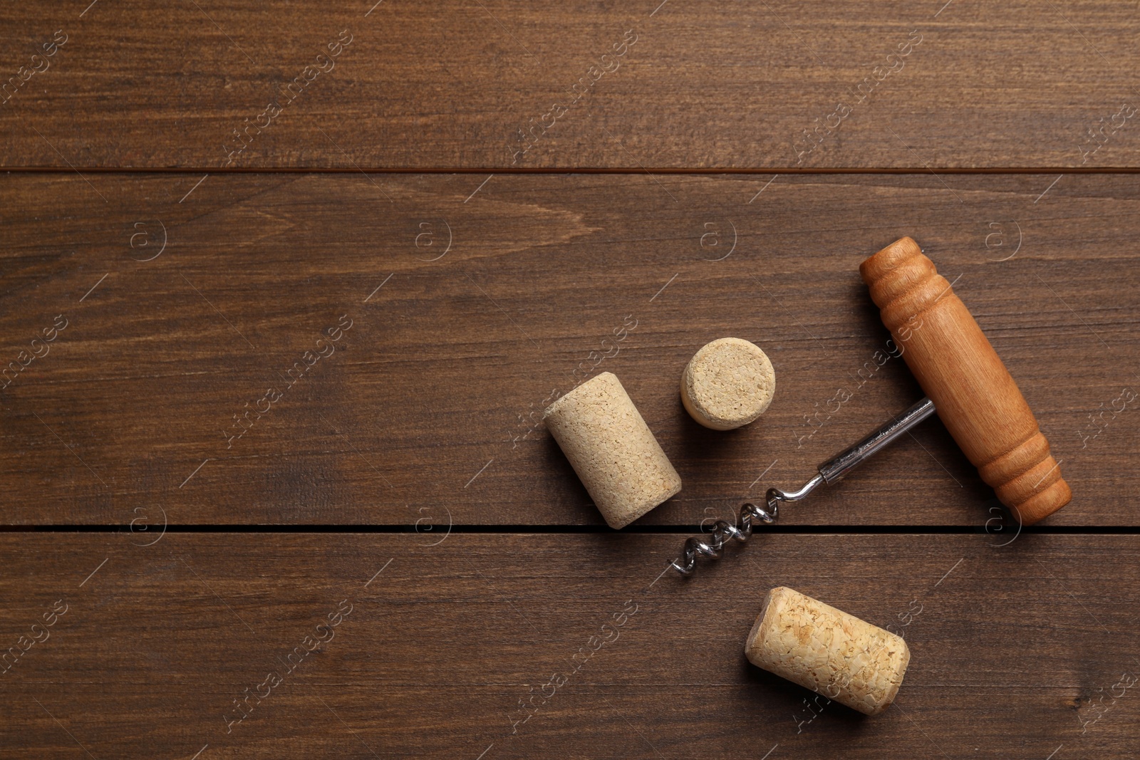 Photo of Corkscrew and corks on wooden table, top view. Space for text