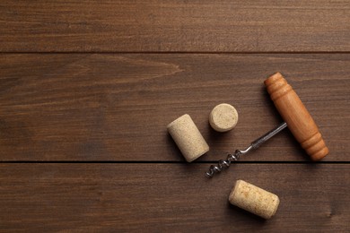 Photo of Corkscrew and corks on wooden table, top view. Space for text