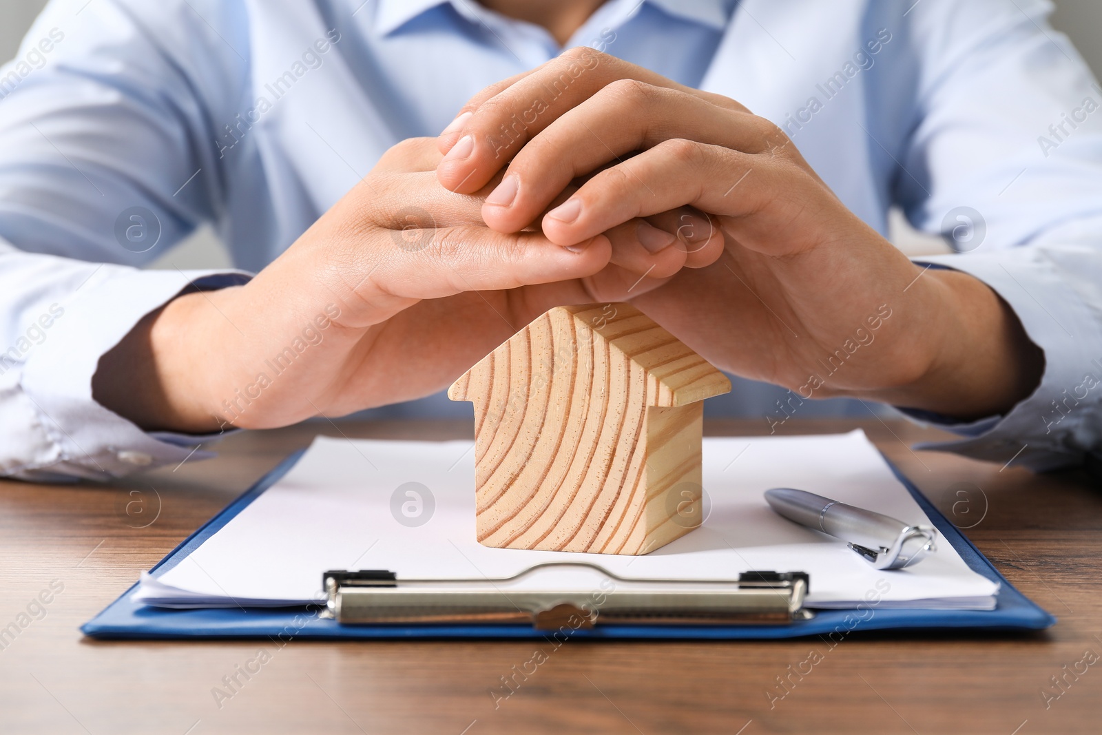 Photo of Real estate insurance. Man with wooden house figure at table, closeup