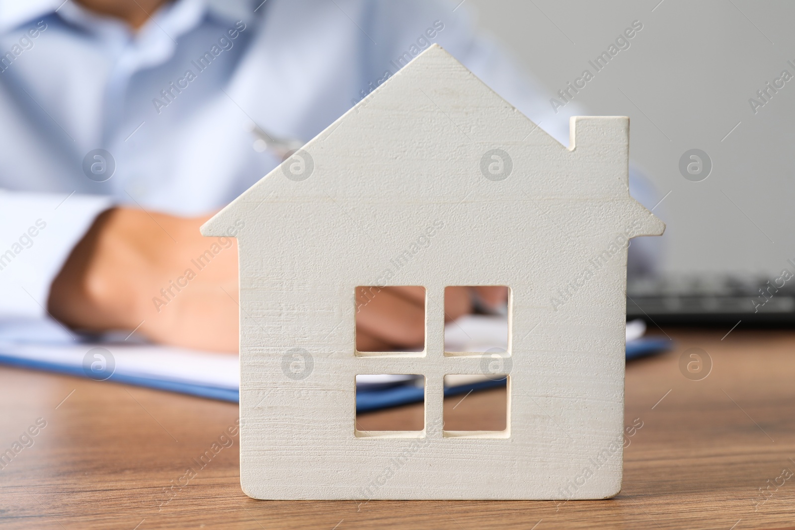 Photo of Real estate insurance. Man writing something at table, focus on wooden house figure