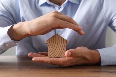 Photo of Real estate insurance. Man with wooden house figure at table, closeup