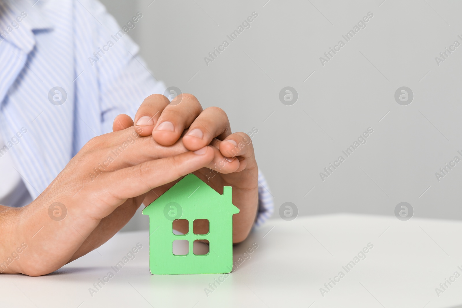 Photo of Real estate insurance. Man with green house figure at light table, closeup. Space for text