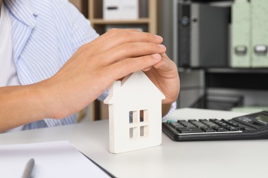 Photo of Real estate insurance. Man with wooden house figure at light table, closeup