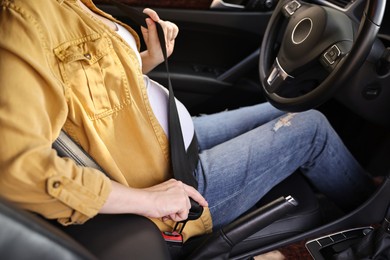 Pregnant woman fastening safety belt in car, closeup