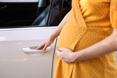 Photo of Pregnant woman opening car door outdoors, closeup