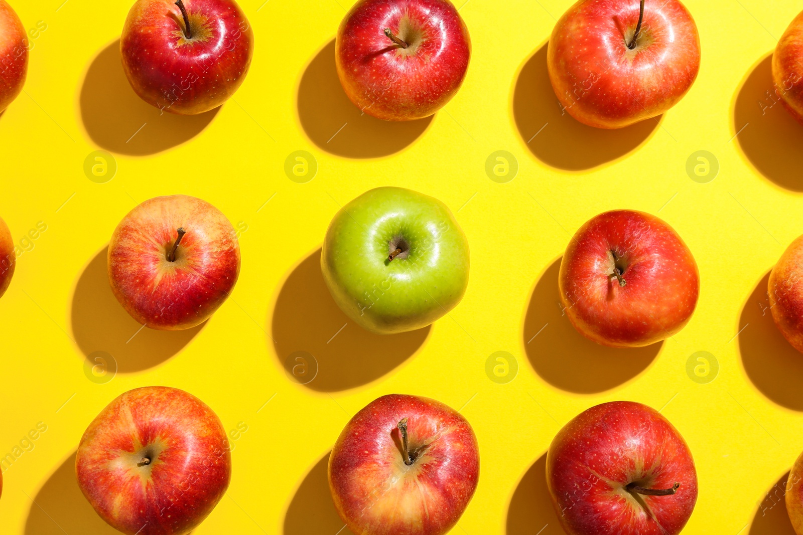 Photo of Flat lay composition with green apple surrounded by red ones on yellow background