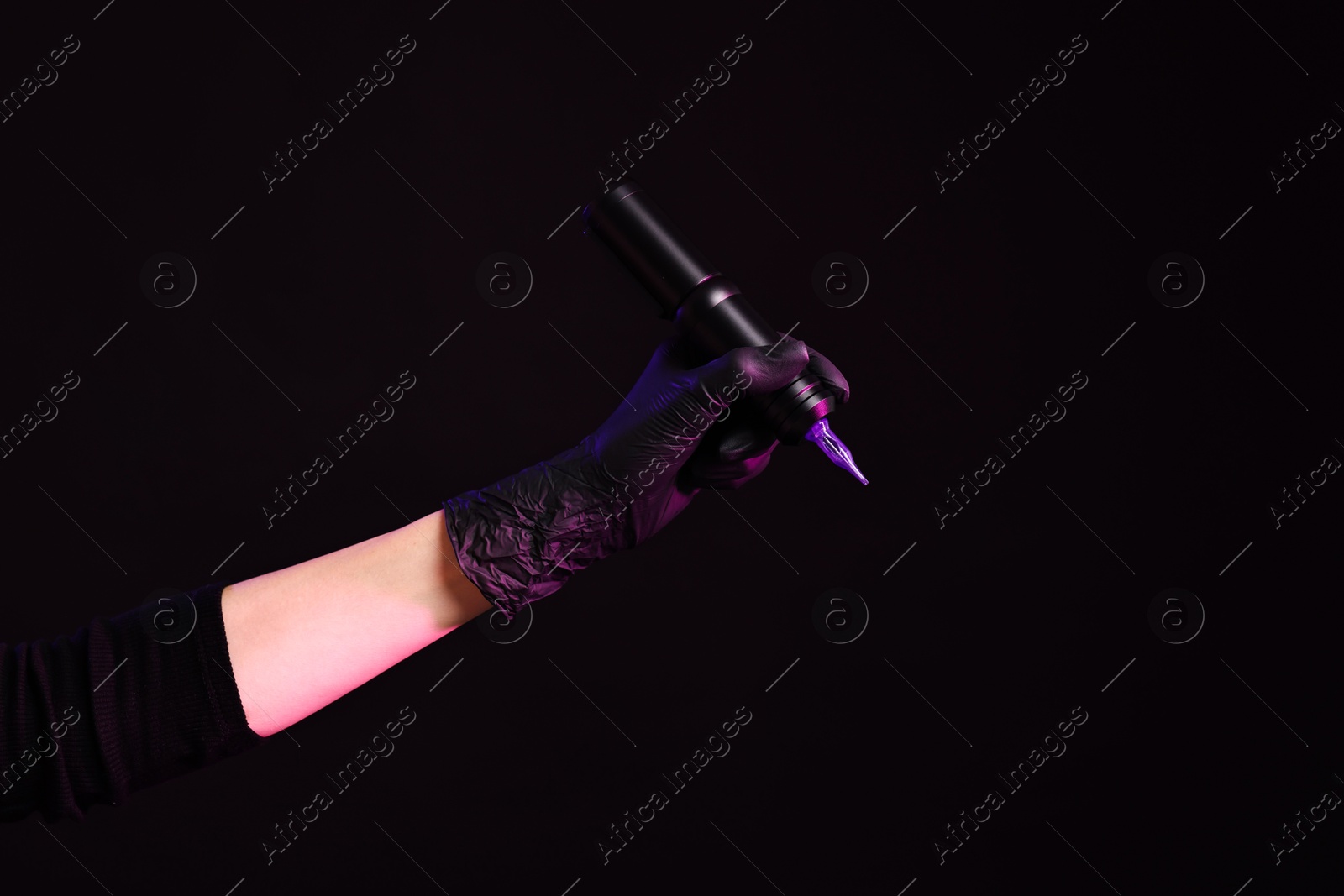 Photo of Professional artist holding tattoo machine on black background in color lights, closeup. Space for text