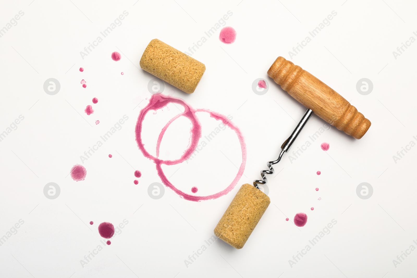 Photo of Corkscrew, corks and red wine stains on white background, top view