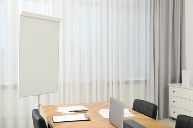 Photo of Flip chart, wooden table and chairs in conference room. Mockup for design