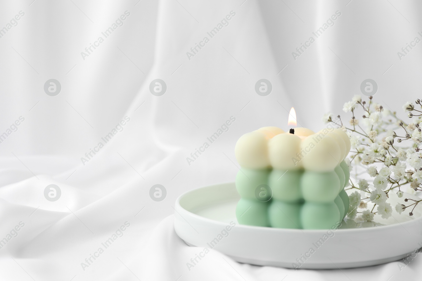 Photo of Stylish bubble candle and gypsophila flowers on white cloth, closeup. Space for text