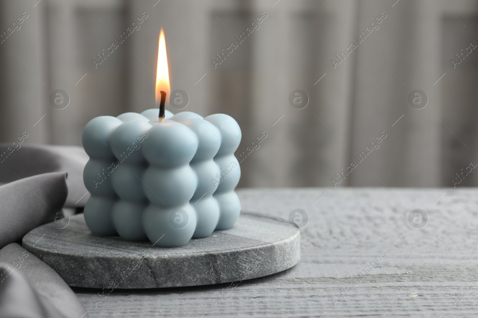 Photo of Burning bubble candle on grey wooden table, closeup. Space for text