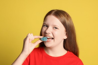 Photo of Teenage girl eating tasty gummy candy on yellow background