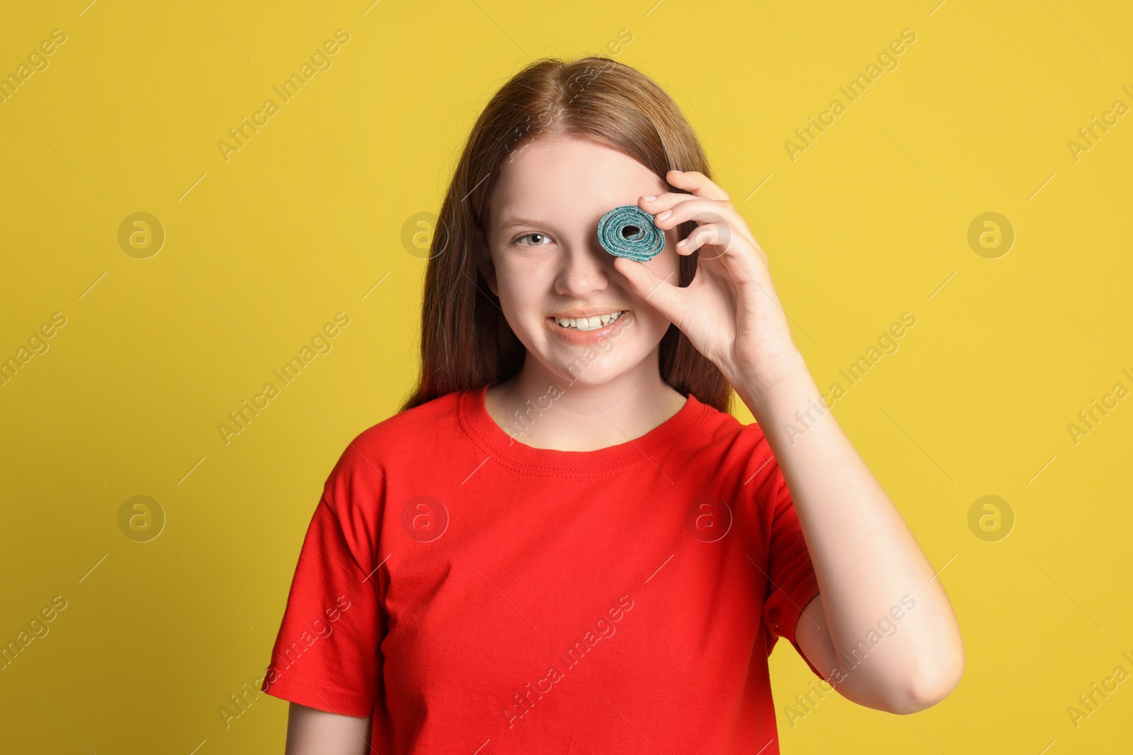 Photo of Happy teenage girl holding tasty gummy candy on yellow background