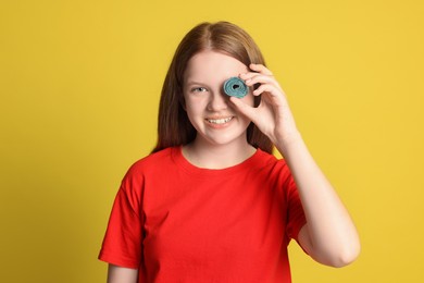 Happy teenage girl holding tasty gummy candy on yellow background