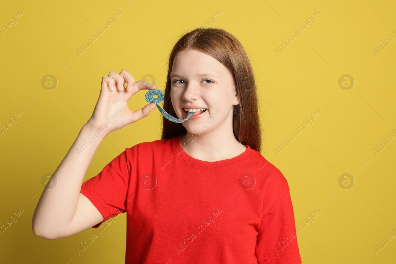 Photo of Teenage girl eating tasty gummy candy on yellow background