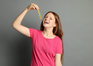 Photo of Happy teenage girl eating tasty rainbow sour belt on grey background