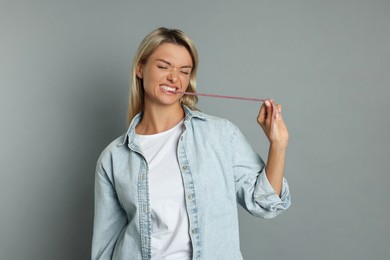 Photo of Young woman eating tasty gummy candy on grey background