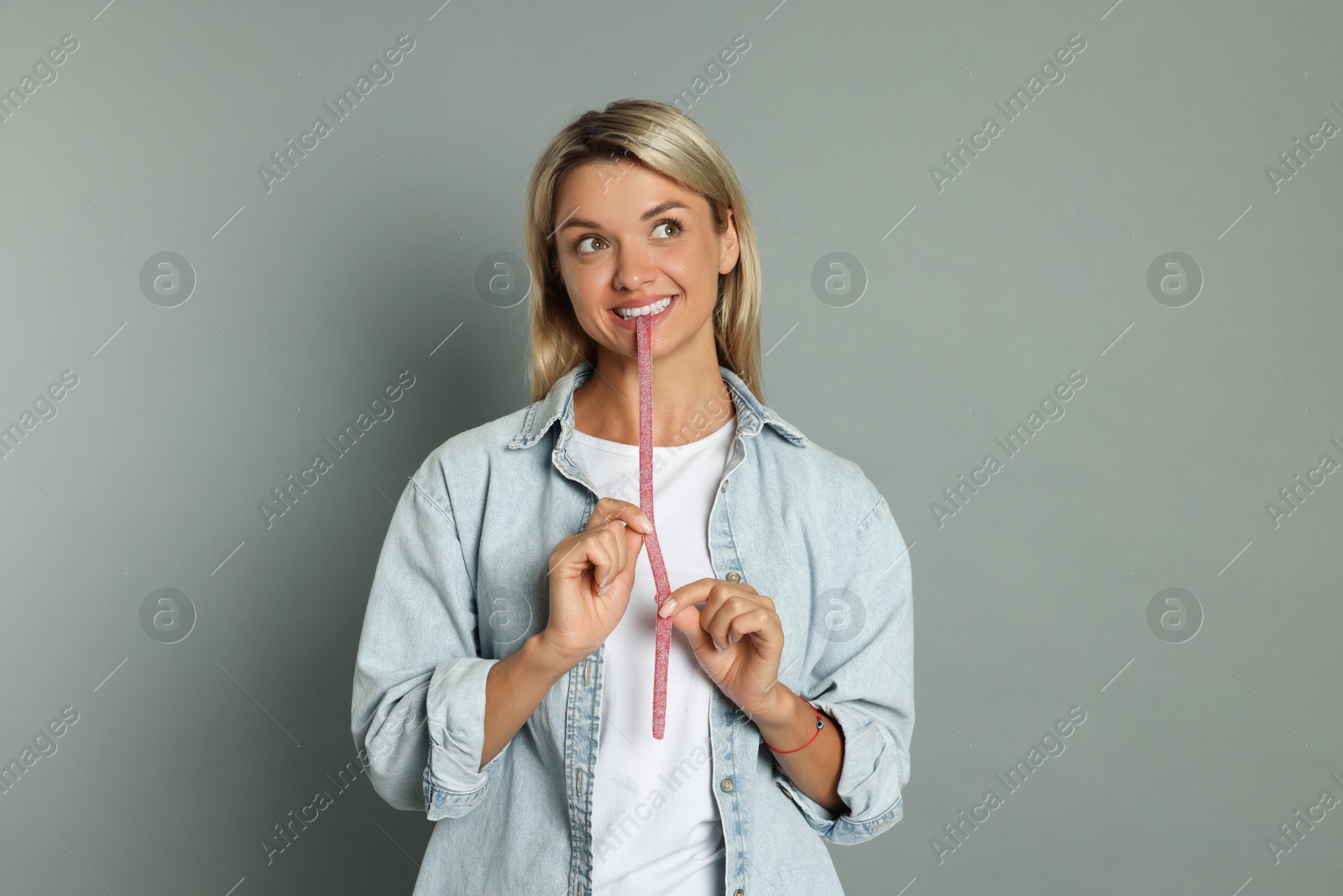 Photo of Young woman eating tasty gummy candy on grey background