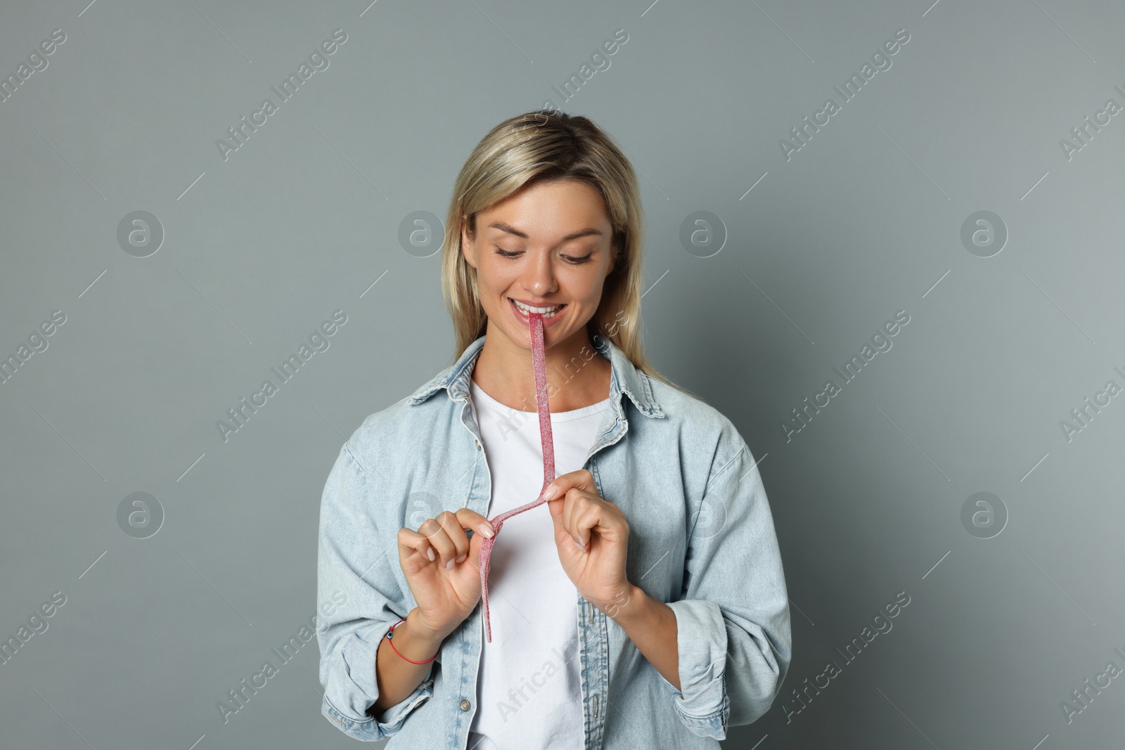 Photo of Young woman eating tasty gummy candy on grey background