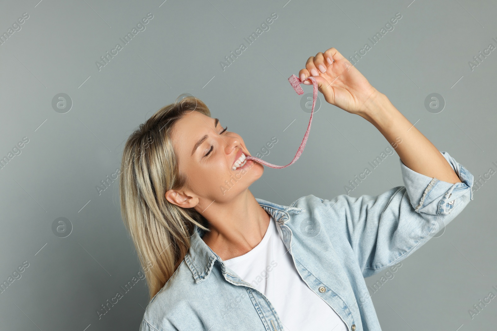 Photo of Young woman eating tasty gummy candy on grey background