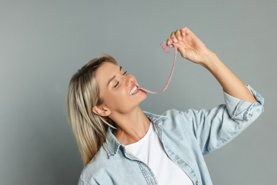 Photo of Young woman eating tasty gummy candy on grey background