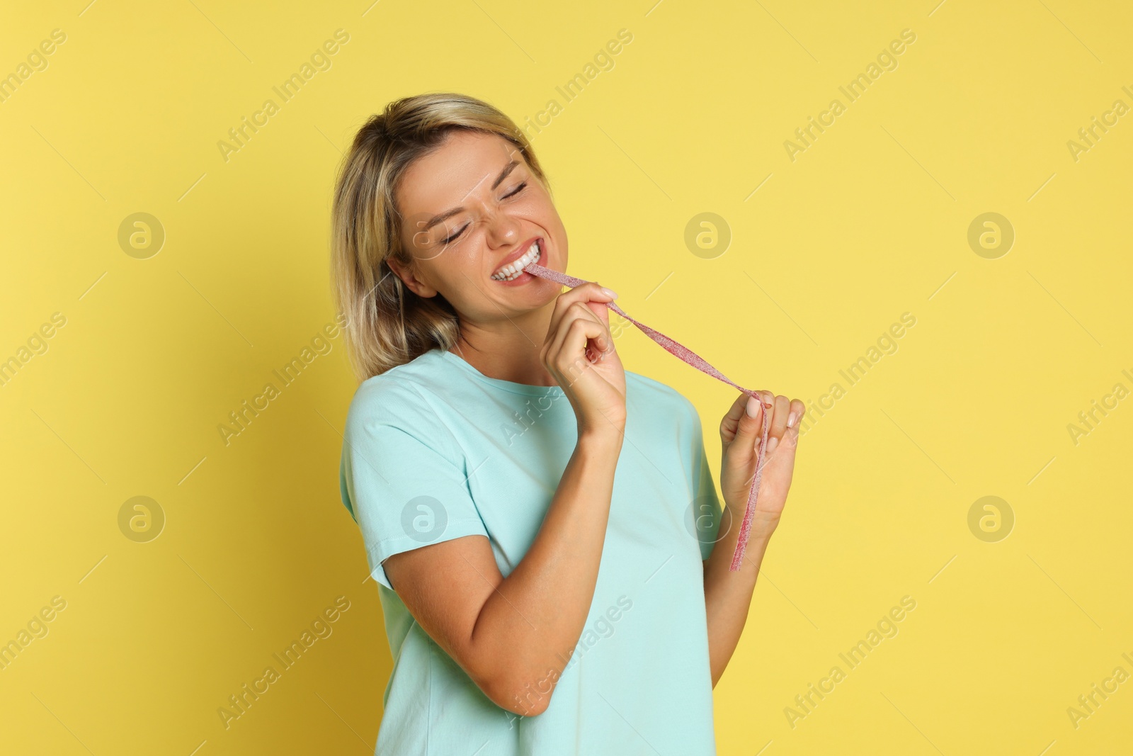 Photo of Young woman eating tasty gummy candy on yellow background