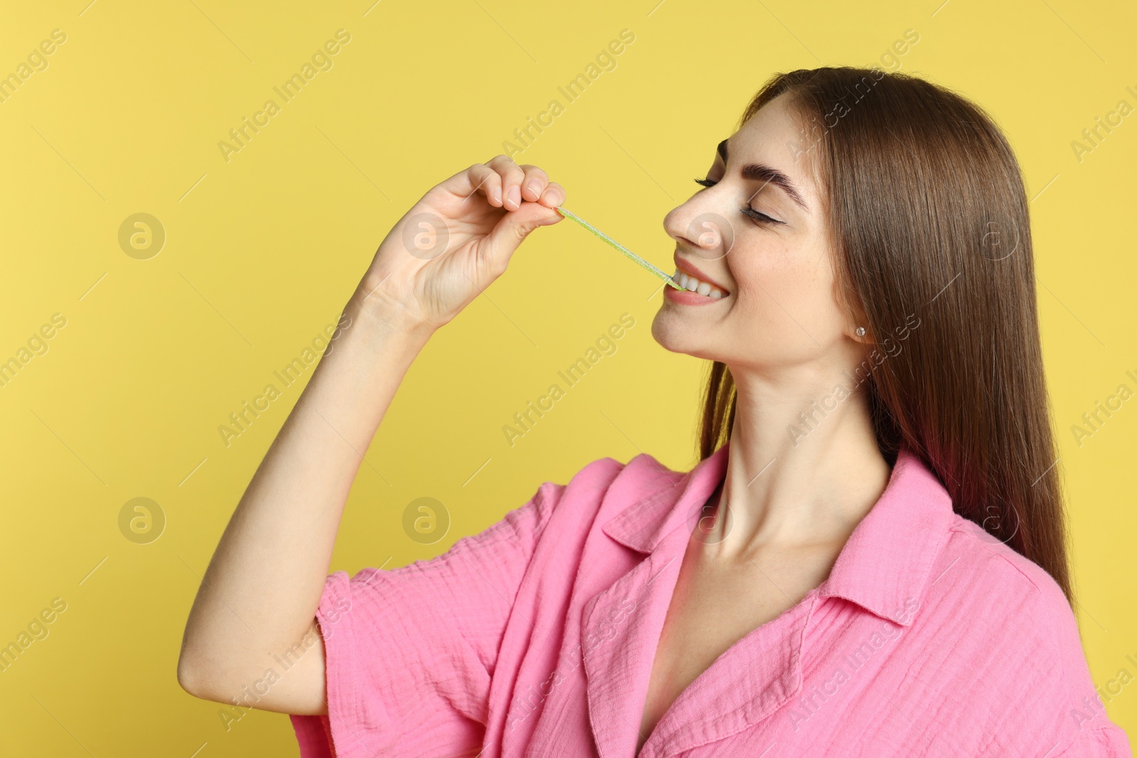 Photo of Young woman eating tasty gummy candy on yellow background