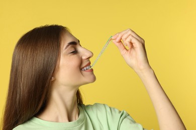 Photo of Young woman eating tasty rainbow sour belt on yellow background