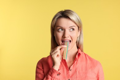 Young woman eating tasty rainbow sour belt on yellow background