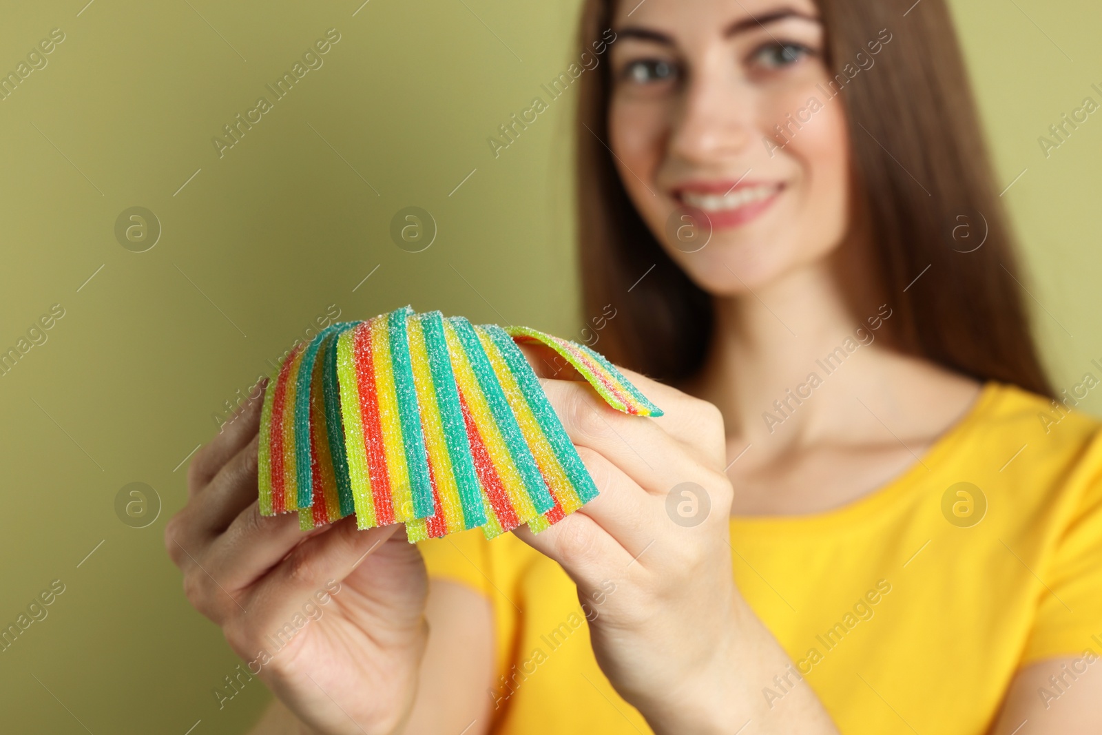 Photo of Happy young woman with tasty rainbow sour belts on olive background, selective focus