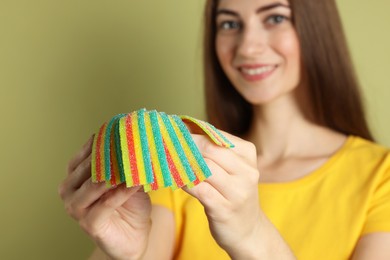 Happy young woman with tasty rainbow sour belts on olive background, selective focus