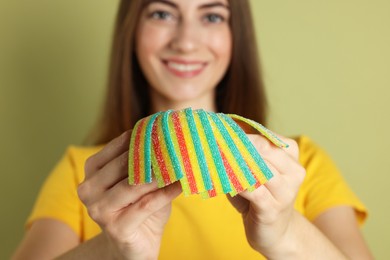 Photo of Happy young woman with tasty rainbow sour belts on olive background, selective focus