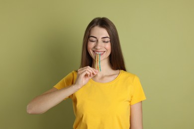 Photo of Young woman eating tasty rainbow sour belt on olive background