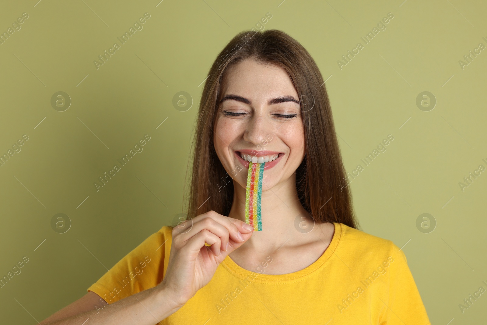 Photo of Young woman eating tasty rainbow sour belt on olive background