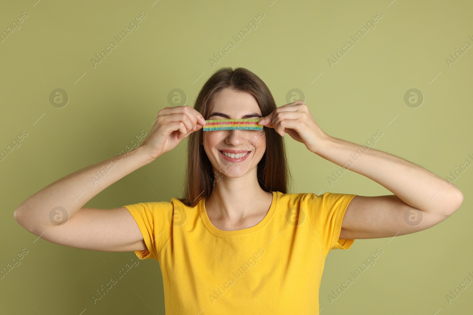 Photo of Young woman closing her eyes with tasty rainbow sour belt on olive background