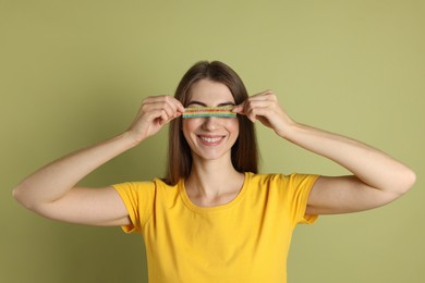 Young woman closing her eyes with tasty rainbow sour belt on olive background