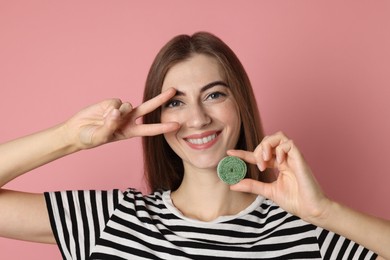 Photo of Happy young woman with tasty gummy candy showing v-sign on pink background