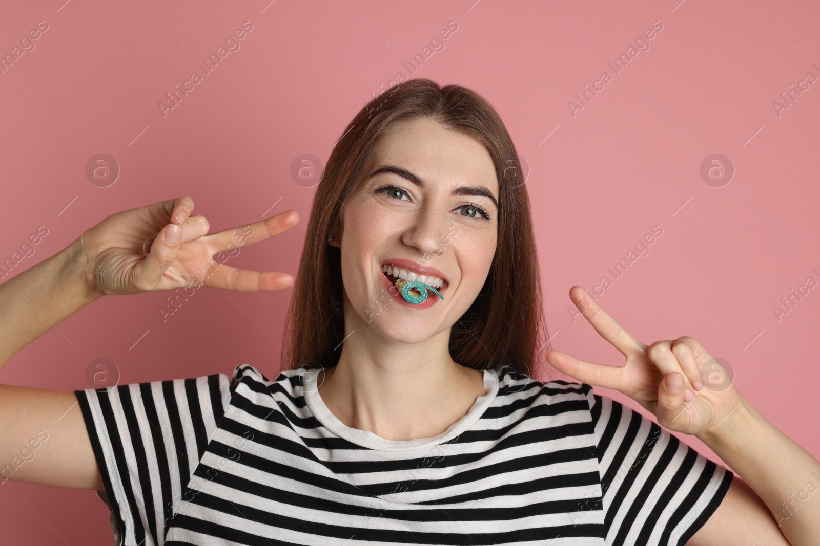 Photo of Young woman with tasty gummy candy showing v-sign on pink background