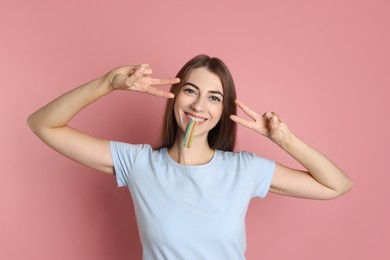 Young woman with tasty rainbow sour belt showing v-sign on pink background