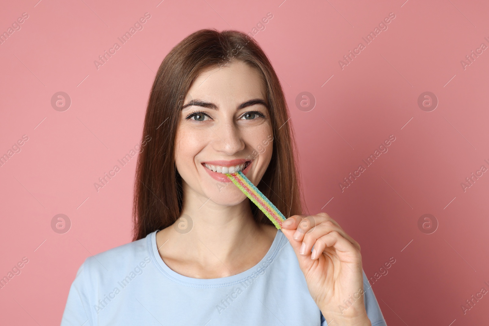 Photo of Young woman eating tasty rainbow sour belt on pink background