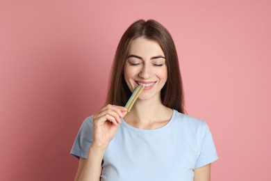 Young woman eating tasty rainbow sour belt on pink background