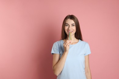 Young woman eating tasty rainbow sour belt on pink background, space for text