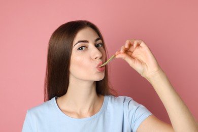 Photo of Young woman eating tasty rainbow sour belt on pink background