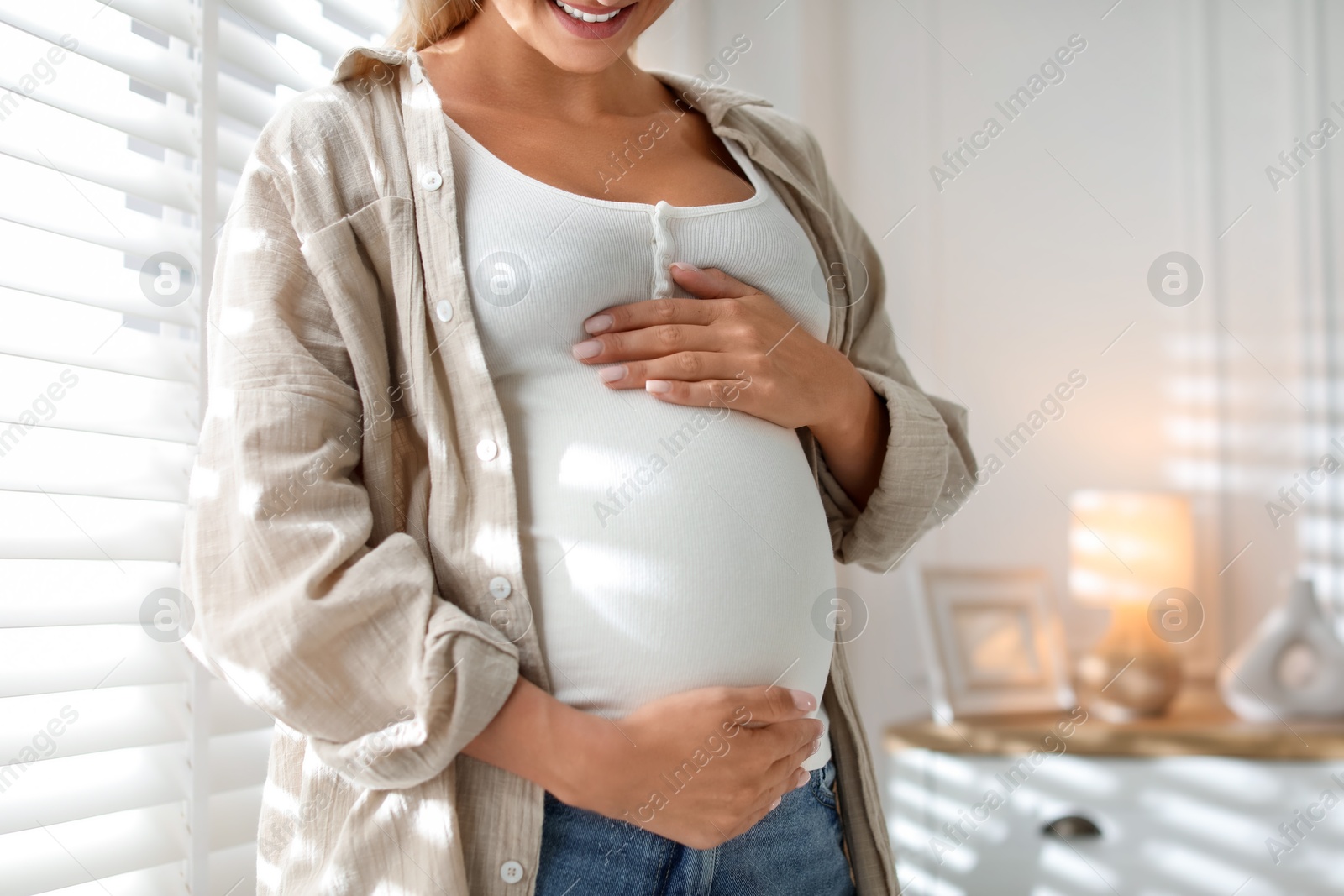 Photo of Pregnant woman near window at home, closeup